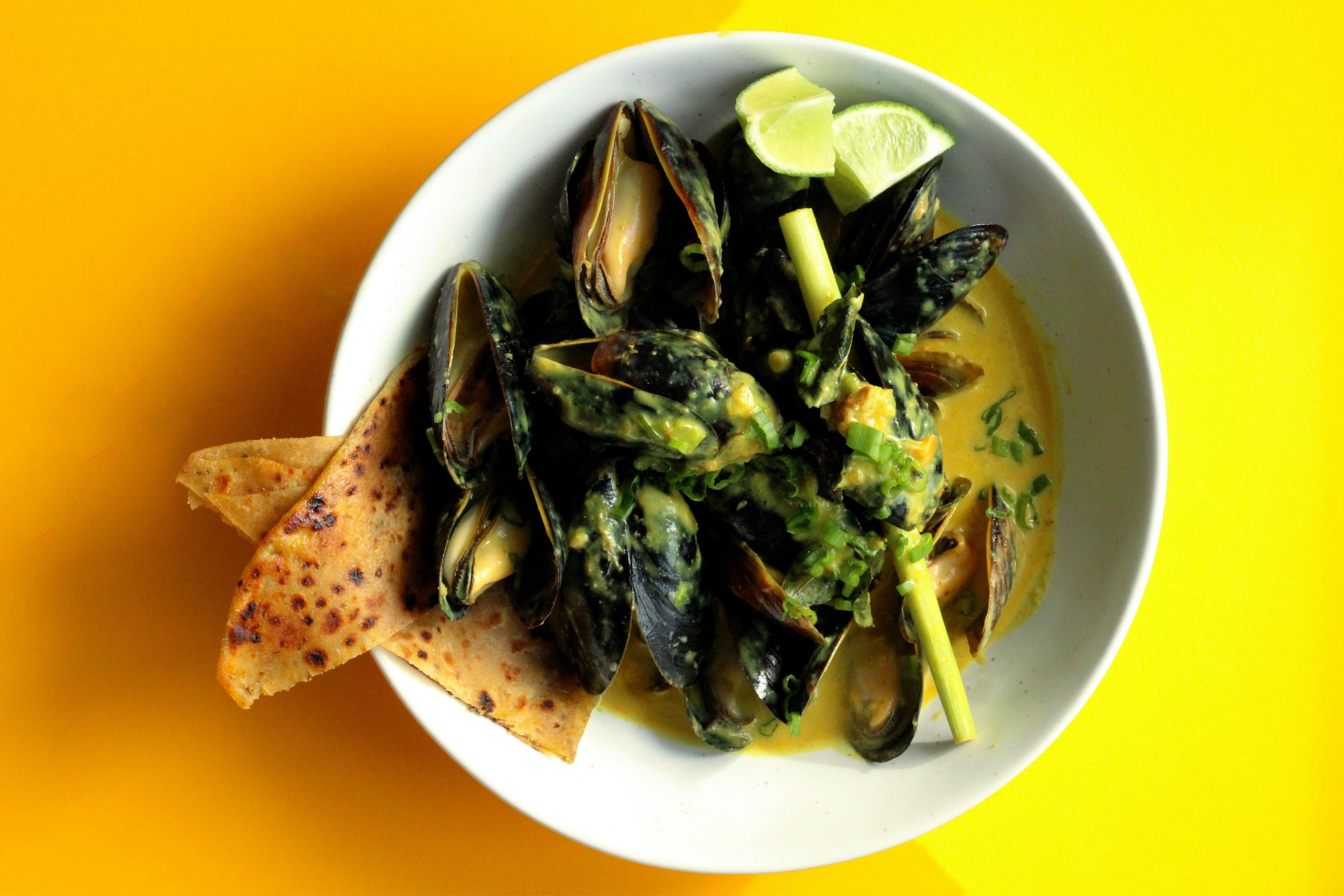 A white bowl of curried mussels against a bright background